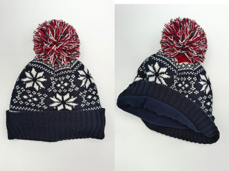 Marineblå strikkelue med hvitt Fair Isle-snøflokmønster og rød/hvit pom-pom. For- og sidevisning.