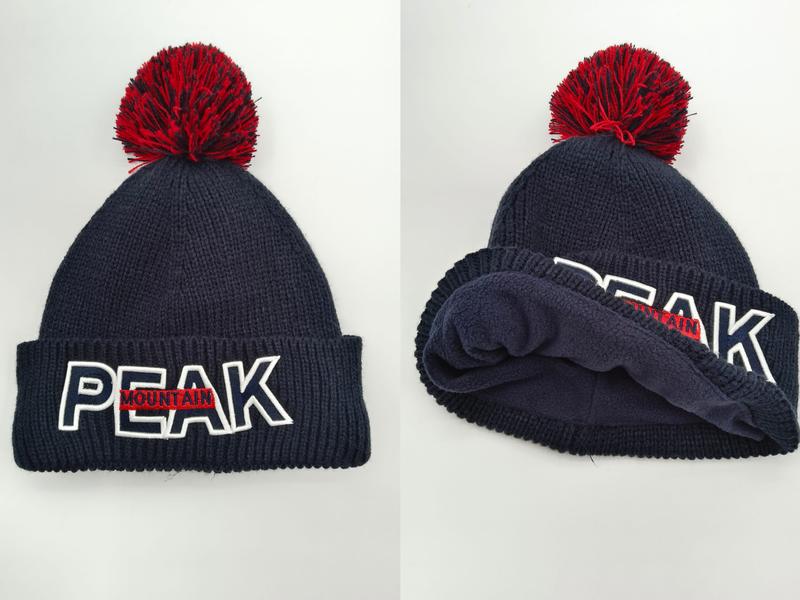 Marineblå strikkelue med rød pompom og brodert PEAK MOUNTAIN-logo på brettet kant.