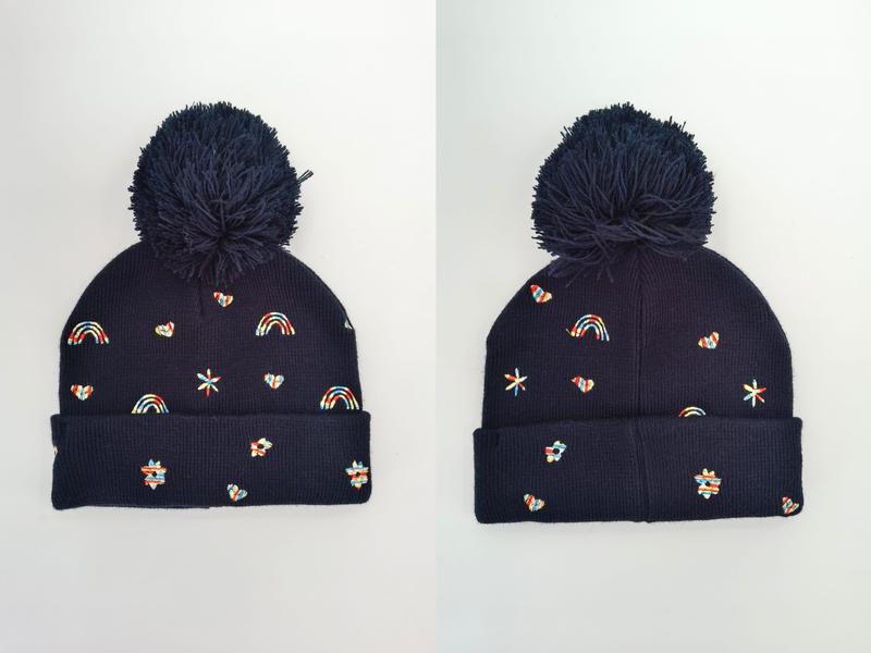 Marineblå strikkelue med stor pom-pom og fargerike broderte regnbuer
