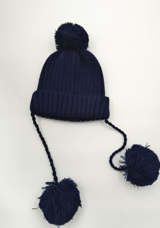 Marineblå ribbestrikket vinterlue med pompom på toppen og to lange flettede bånd med store pompomer i endene.