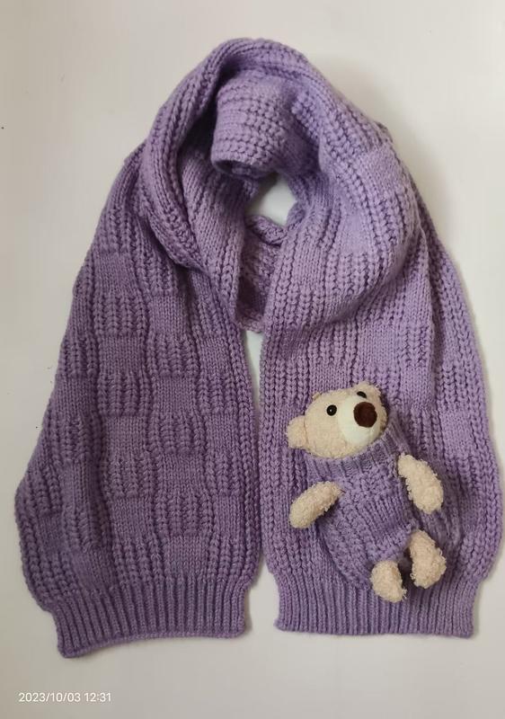 Lilla grovstrikket skjerf med kosebamse i lomme – grossist tilgjengelig. Myk lavendel vinteraccessoar.