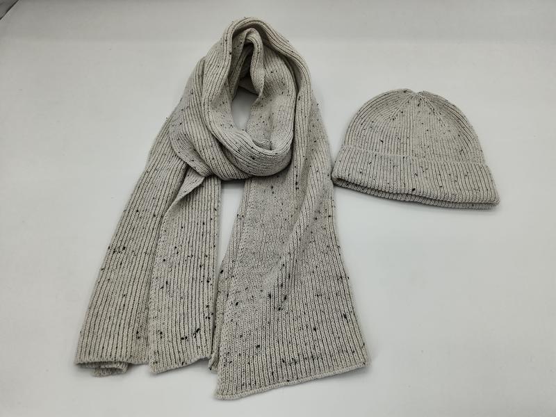Lysegrå ribbestrikket skjerf og beanie med flekkmønster som sett forfra på hvit bakgrunn.