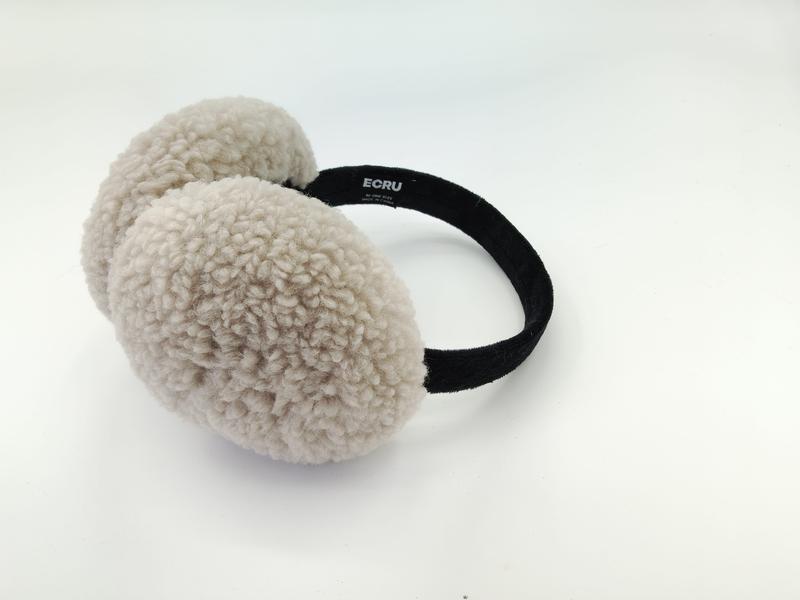 Kremhvite ørevarmer i sherpa fleece med svart hodebånd. Fluffy teksturerte øreputer på hvit bakgrunn.