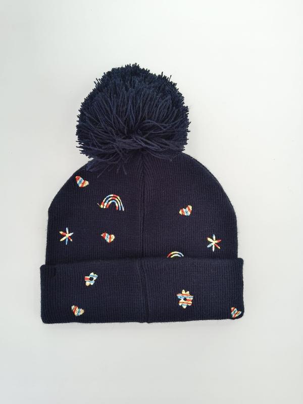 Marineblå strikket vinterlue med stor pom-pom og fargerike broderte regnbuer