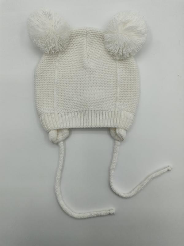 Elfenbenshvit strikket babylue med to pompomer på toppen og lange bindebånd under haken.