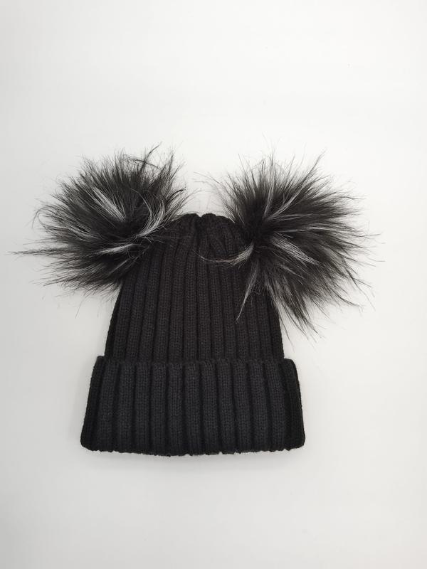 Svart ribbestrikket lue med to store kunstpels-pompomer på toppen.