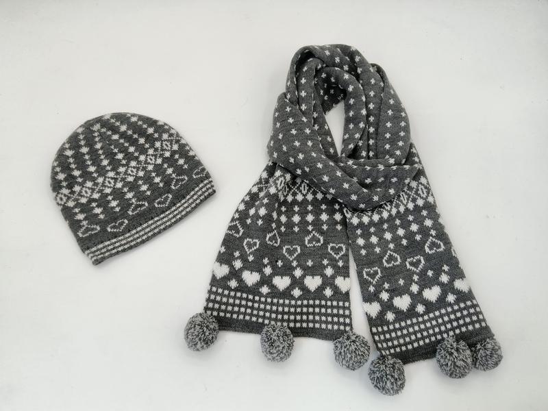 Grå og hvit Fair Isle-strikket lue og skjerf-sett med hjertemønster og pom pom-ender.