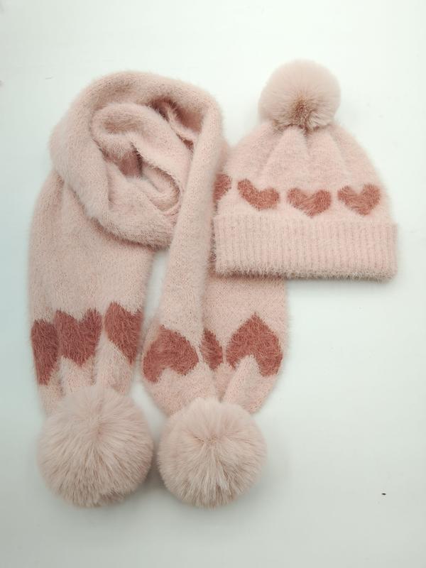 Rosa fluffy strikket vinterlue og skjerf med hjertemønster og pompommer på hvit bakgrunn.