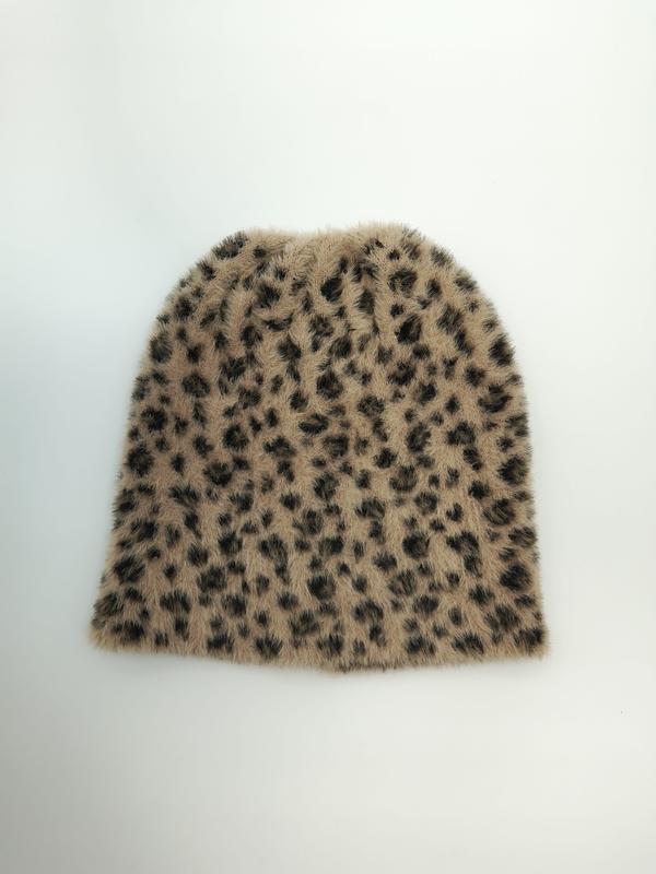 Flat lay av en beige og mørkebrun leopardmønstret fuzzy strikket lue på hvit bakgrunn.