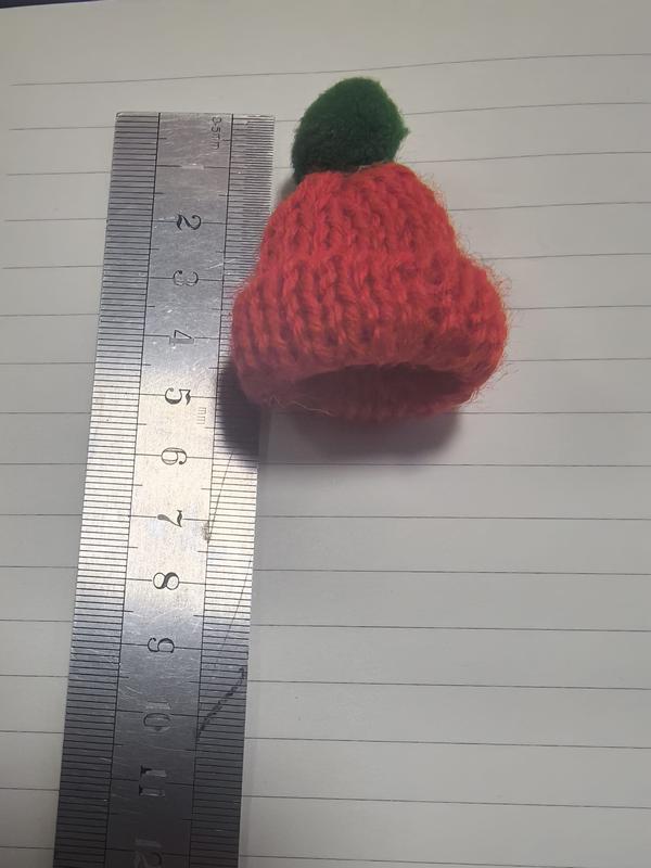Liten rød strikkelue i miniformat med grønn pom-pom