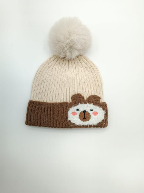 Kremhvit og brun strikket barnelue med pompom og søtt bjørnefjes på bremmen.