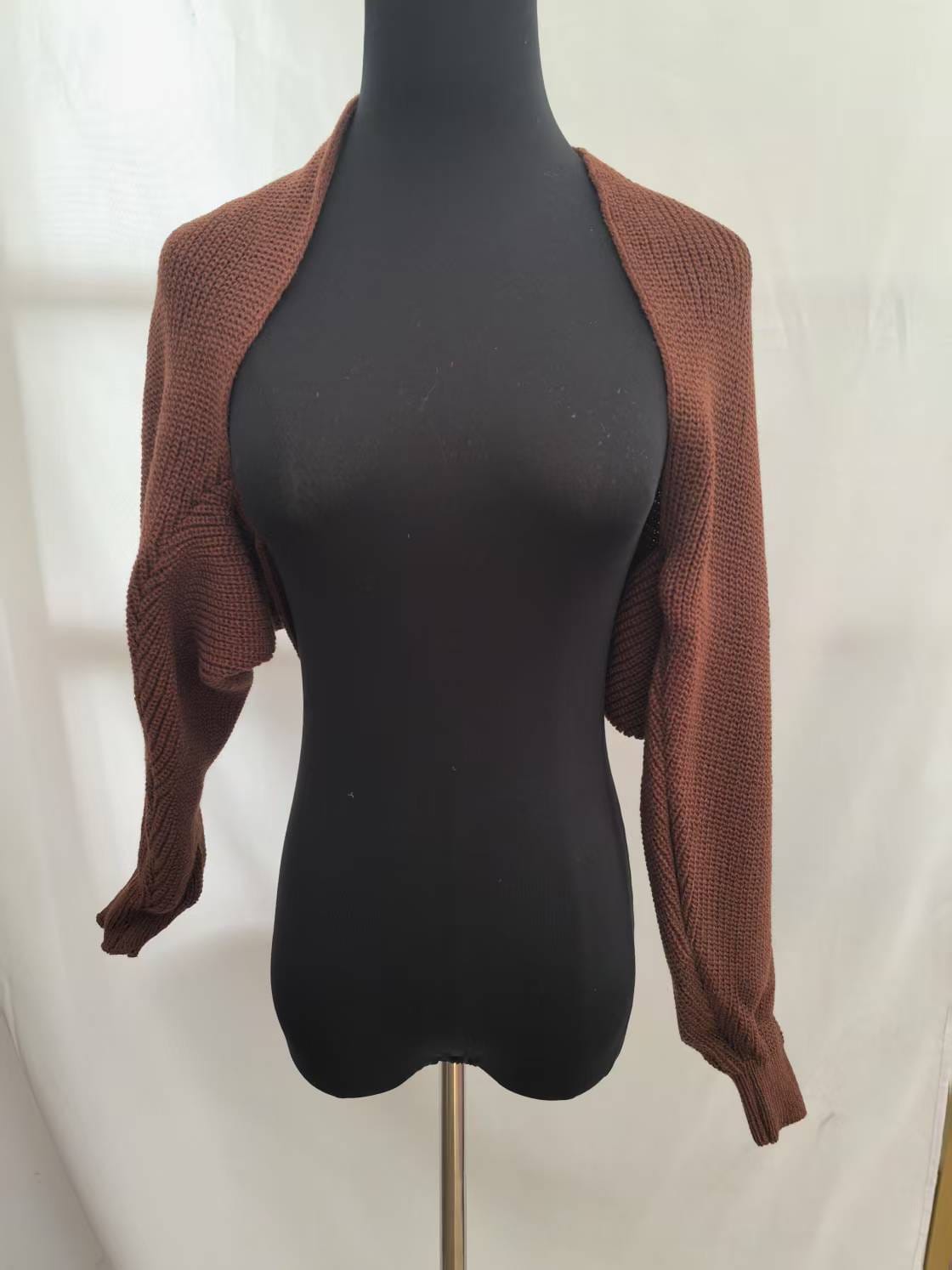 Brun, grovstrikket bolero-cardigan med åpen front og lange ermer, vist på svart mannequin mot hvit bakgrunn.