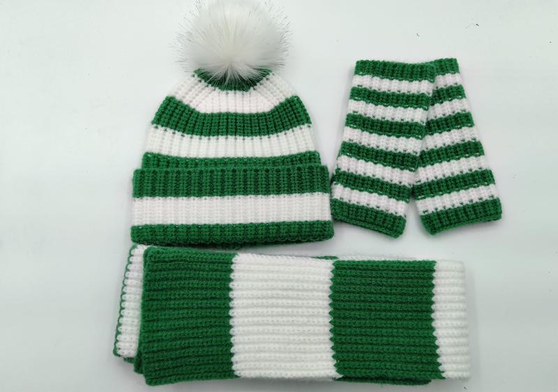 Grønn og hvit stripete vinterset i strikk med pompom-lue, skjerf og votter på hvit bakgrunn.