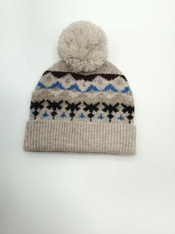 Havregryn strikket lue med Fair Isle-mønster i blått og svart, pyntet med en fluffy kremfarget pom-pom.